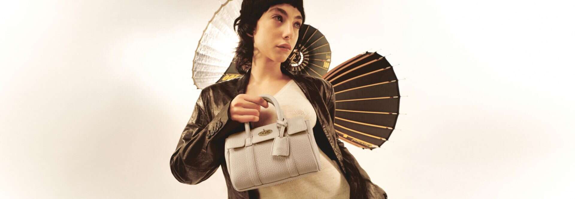 Elegant woman holding a designer handbag with traditional Japanese parasol in the background.