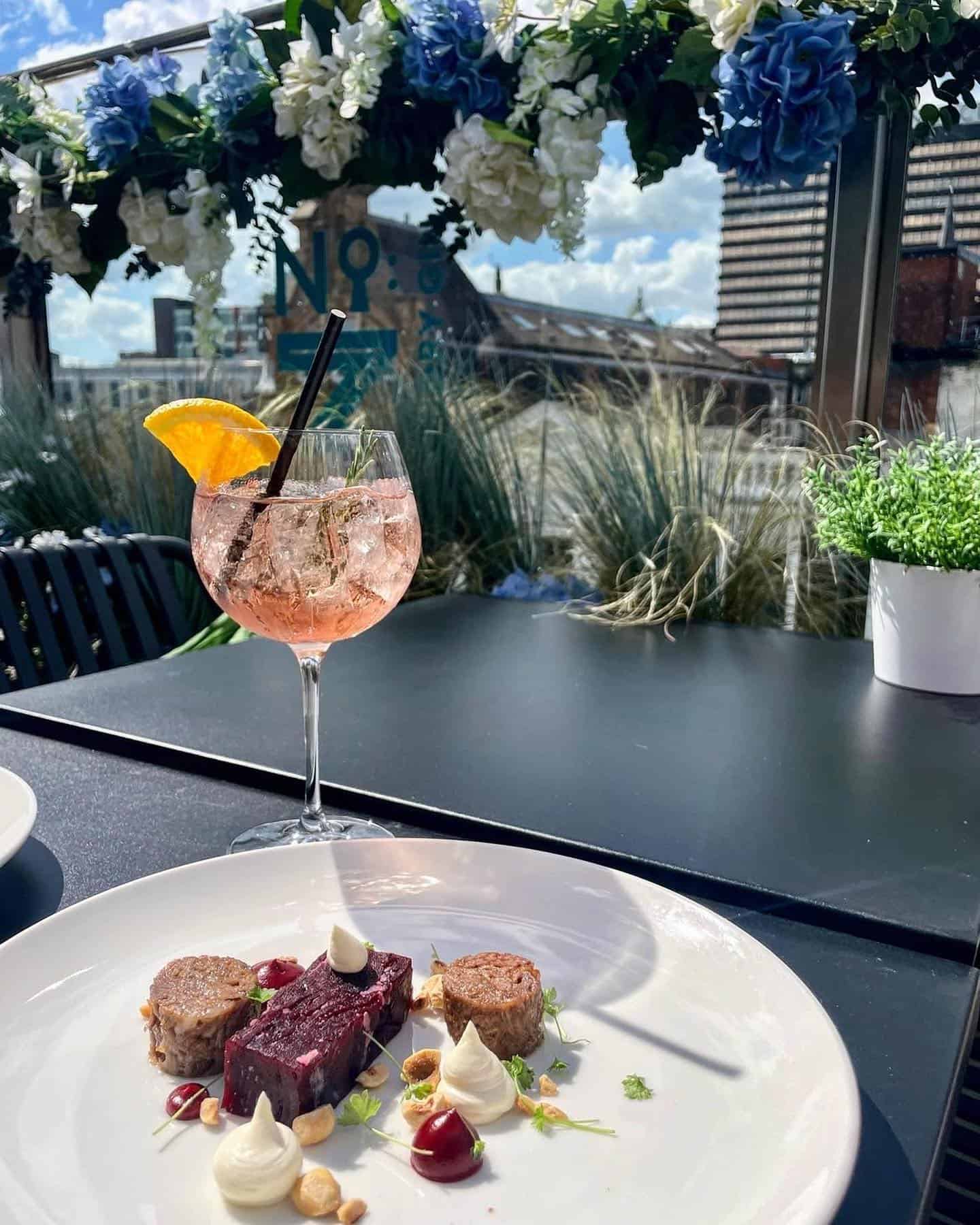 Outdoor dining with a refreshing pink cocktail and gourmet dishes at Victoria Leeds rooftop.