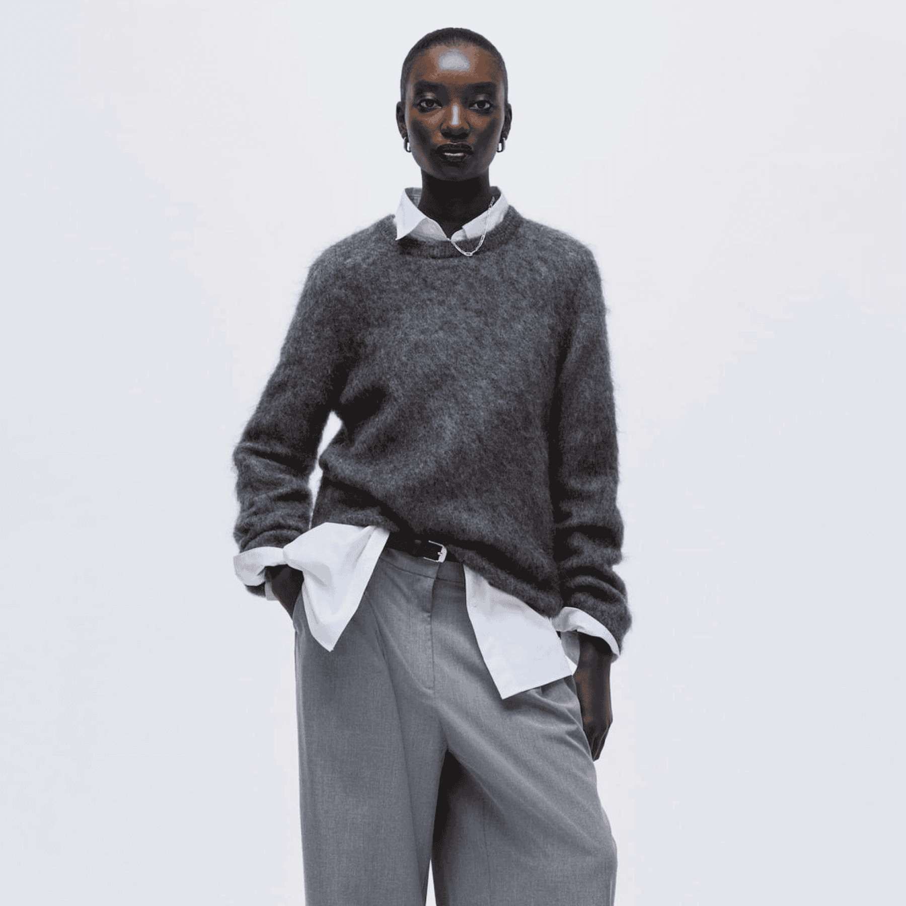 Woman wearing grey knit sweater and white shirt, stylish casual look.