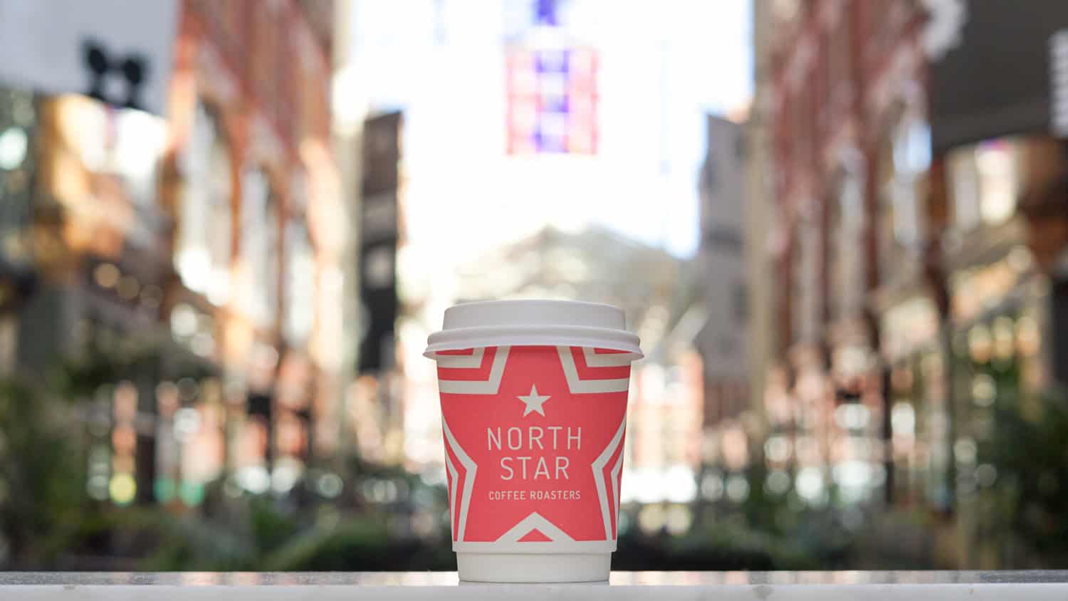 Bright red North Star coffee cup with city street background, promoting Victoria Leeds shopping dest.