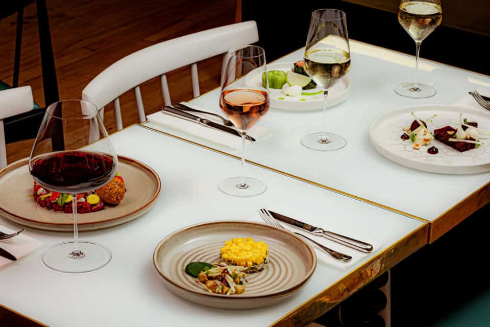 Elegant tasting menu with wine glasses and gourmet dishes on a white table.