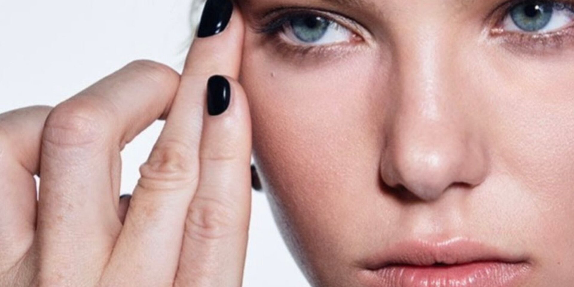 Close-up of a woman's face with flawless makeup and black nail polish.