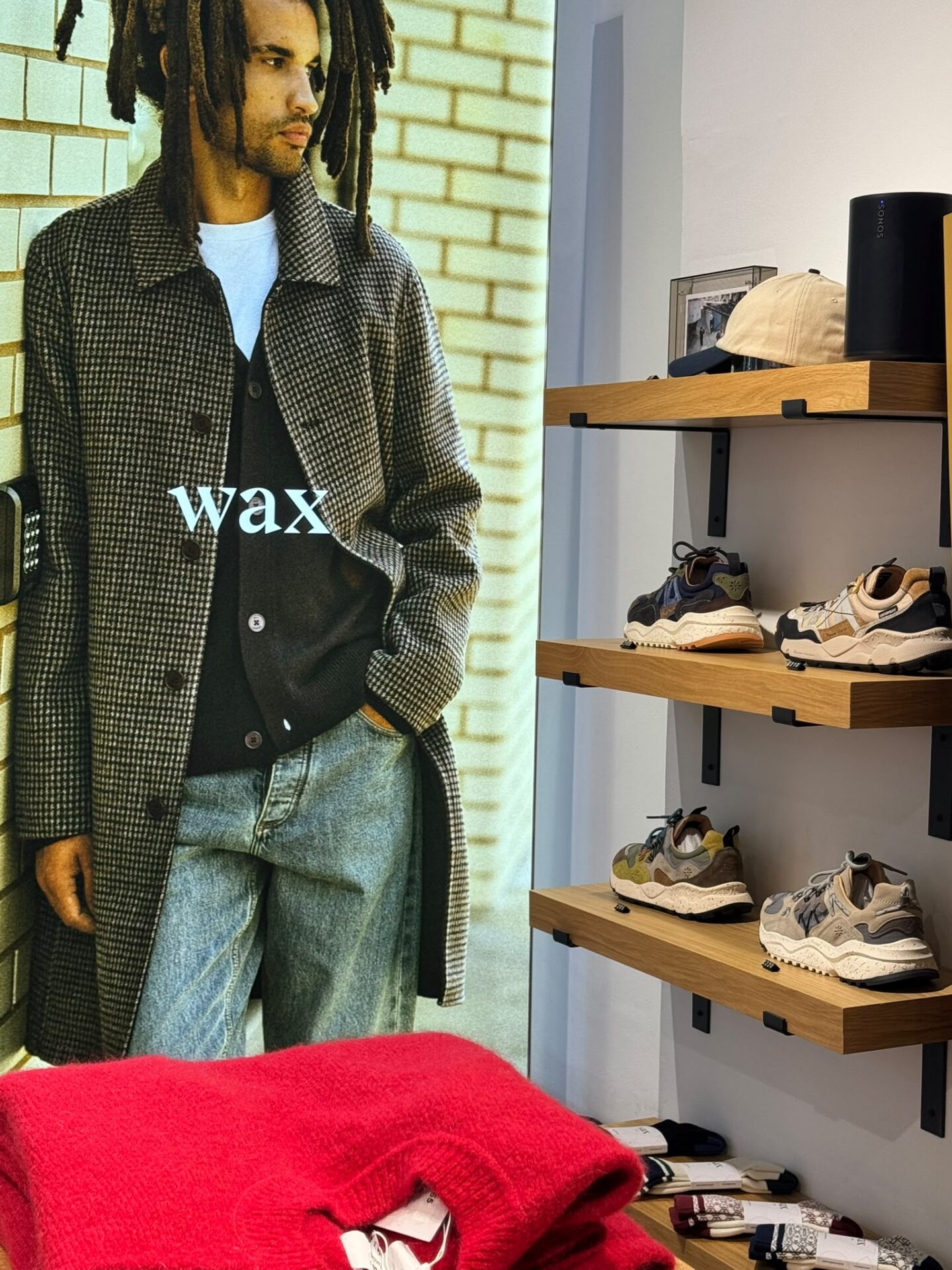 Wax London model in store wearing checkered overcoat and light blue sweater.