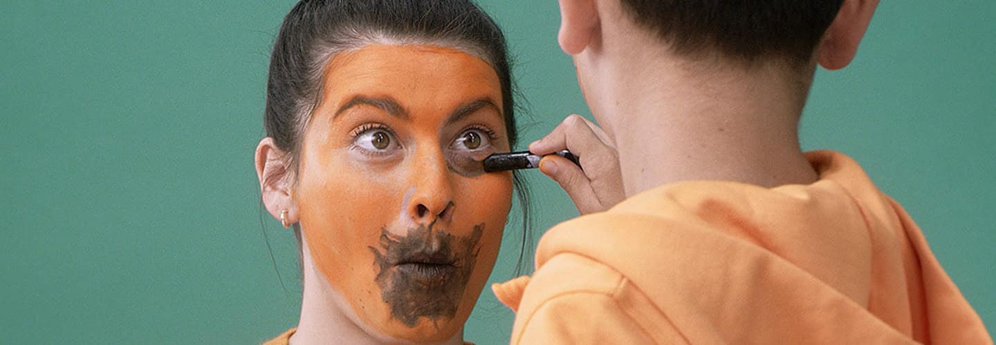 Woman with face paint and makeup artist applying makeup.