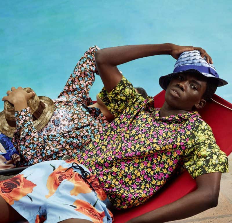 Relaxed woman lounging by the pool in colourful floral attire and a sun hat.