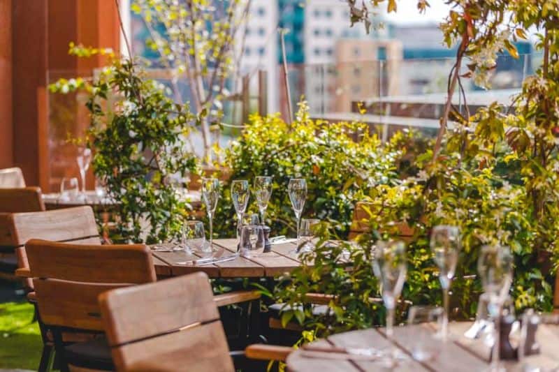 Elegant outdoor dining space at Victoria Leeds with wooden tables and lush plants for al fresco meal.