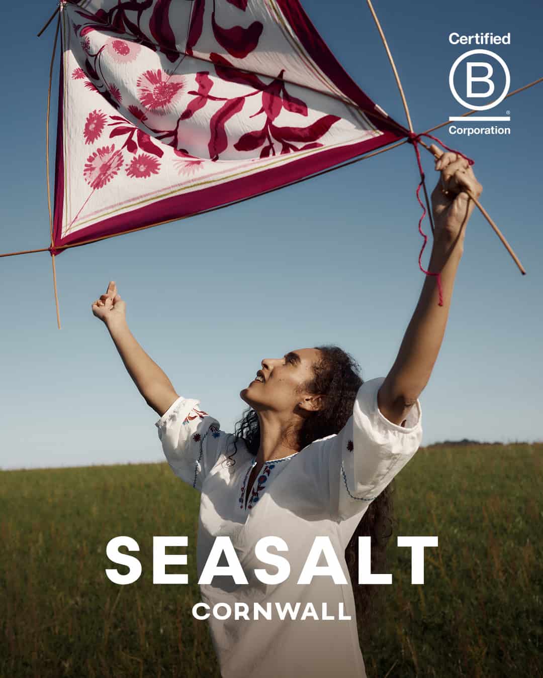 Girl flying a pink floral kite outdoors in a green field on a sunny day.