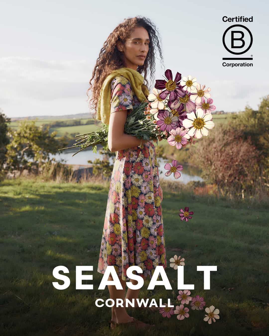 Elegant woman holding a bouquet of flowers outdoors in a floral Seasalt dress.
