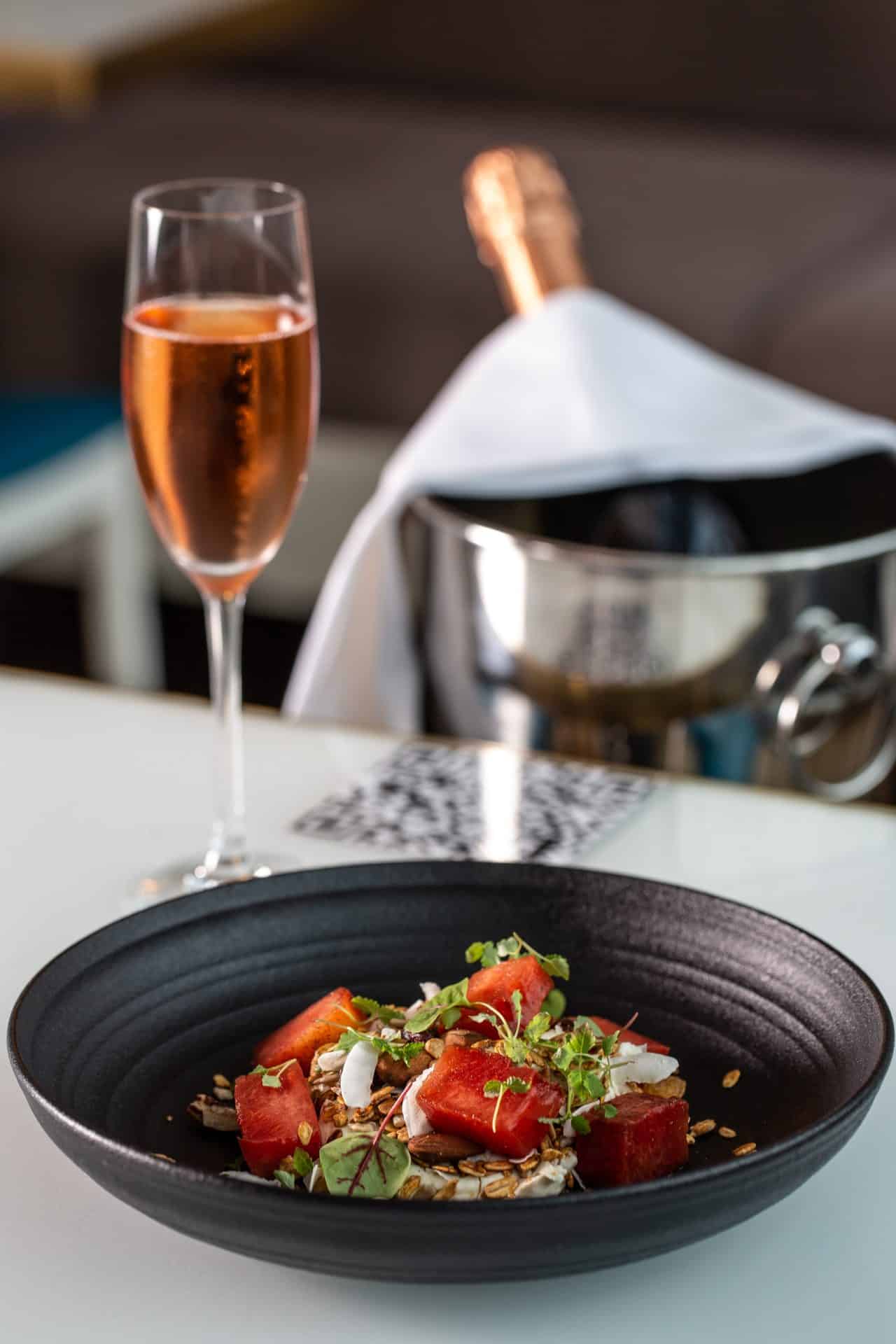 Gourmet watermelon salad with microgreens and nuts, served with a glass of rosé wine.