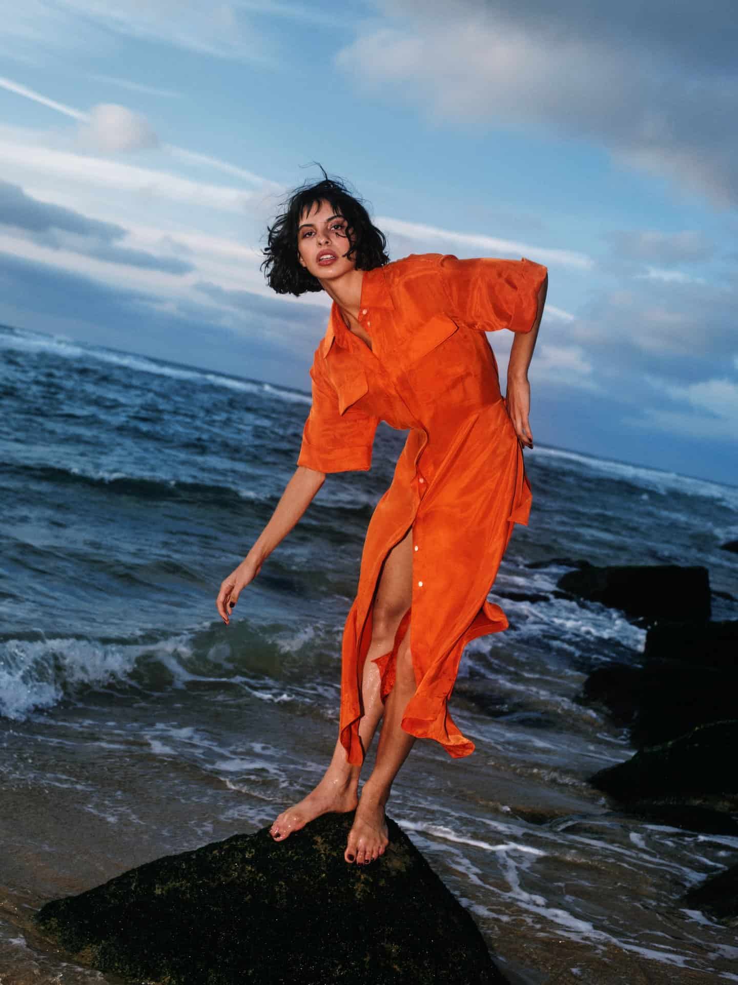 Victoria Leeds model in vibrant orange dress by the seaside.