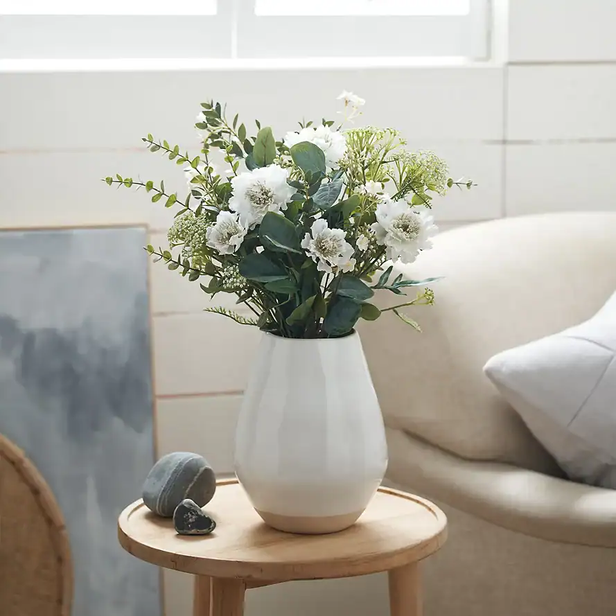 Elegant white vase with fresh white and green floral arrangement in a modern living room.