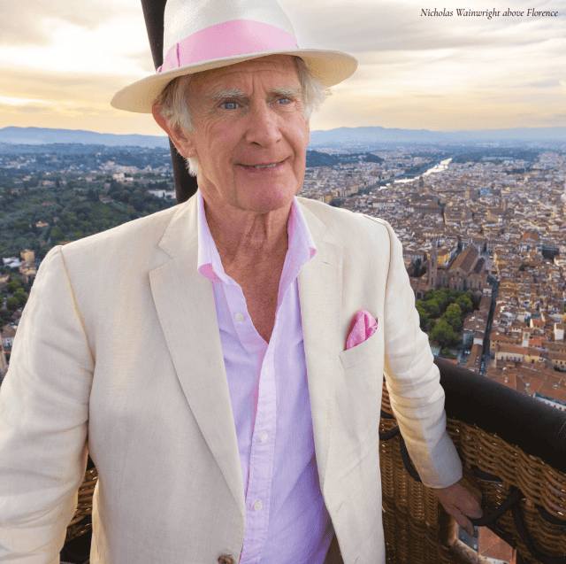 Elegant man in a white suit and pink hat overlooking a cityscape, showcasing luxury jewellery and hi.