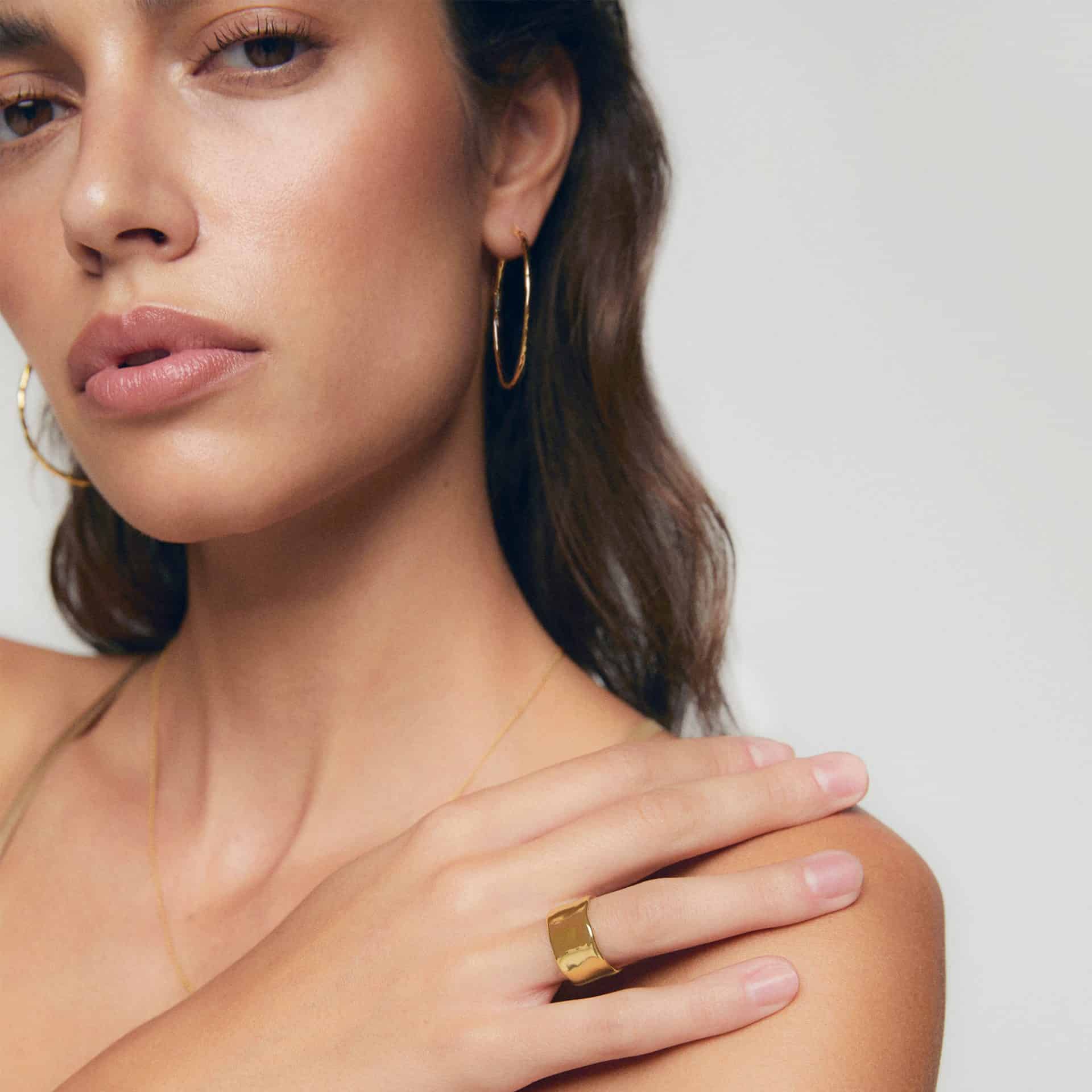 Close-up of a woman wearing gold hoop earrings and a gold ring, showcasing luxury jewelry.