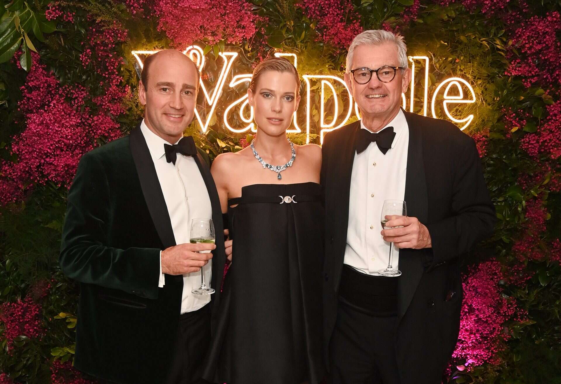 Elegant group of three at Victoria Leeds event, dressed in formal evening wear, with floral backdrop.