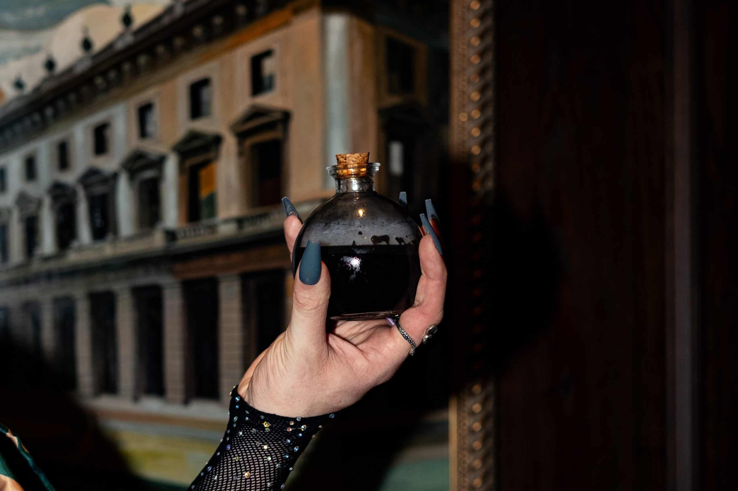 Hand holding a small potion bottle with dark liquid, perfect for Halloween celebrations at Victoria.