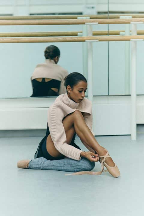 Ballet dancer tying her pointe shoes in a dance studio.