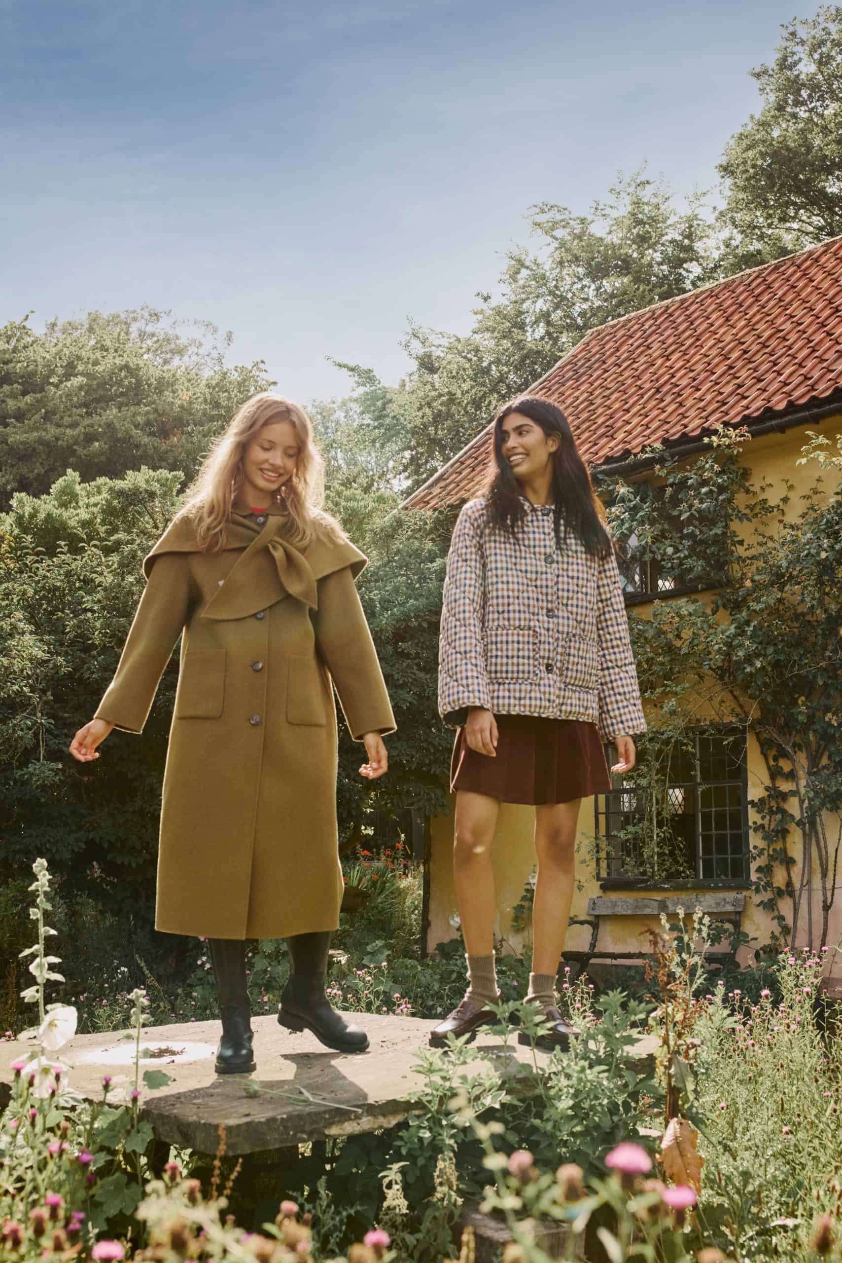 Two women in stylish coats standing outdoors in a garden setting.