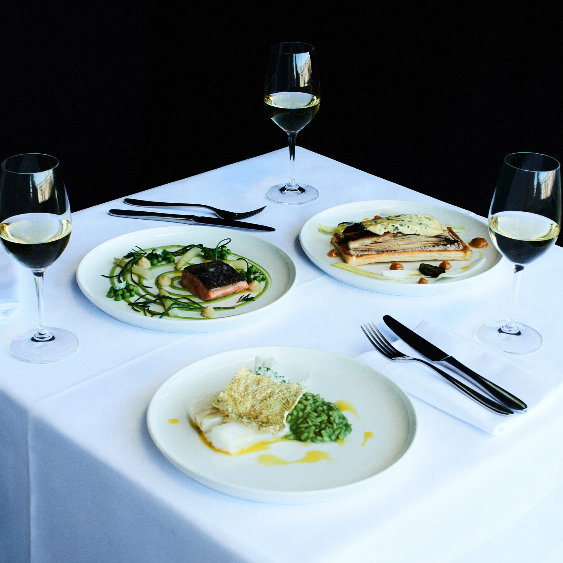 Elegant tasting menu with seafood and meat dishes, paired with white wine, served on a white tablecl.