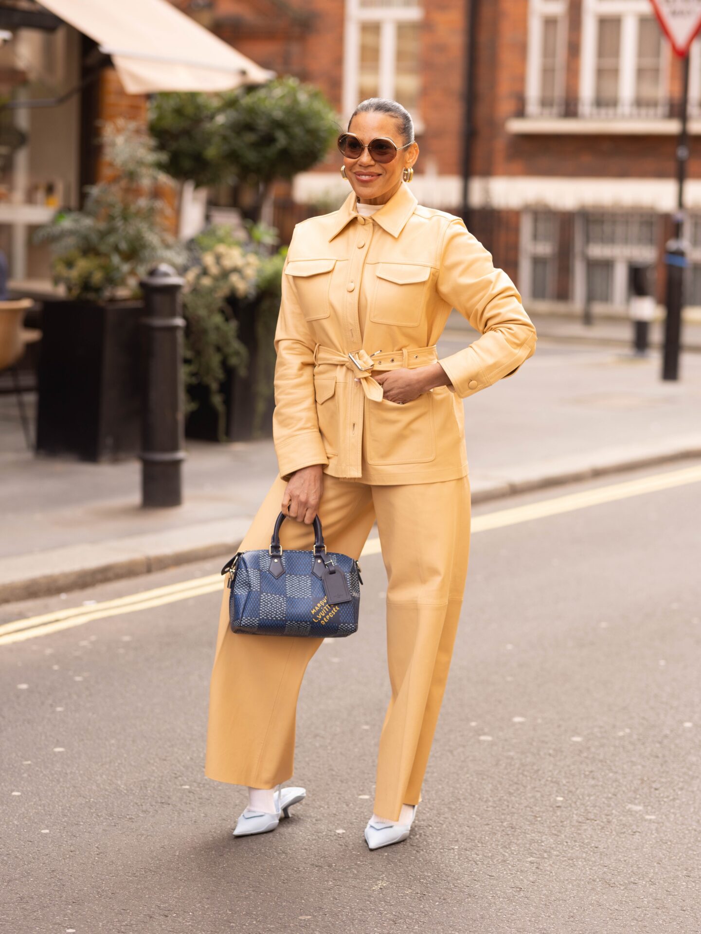 Woman in beige suit with blue handbag on city street.