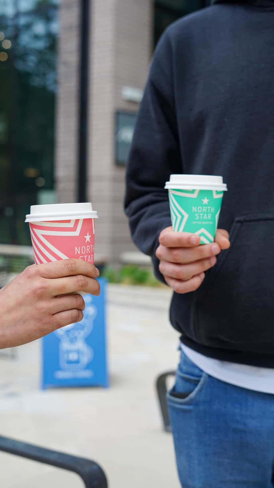 Two people holding North Star coffee cups outside Victoria Leeds.