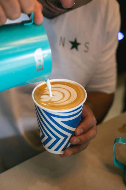 Barista pouring milk into a coffee cup with latte art design.