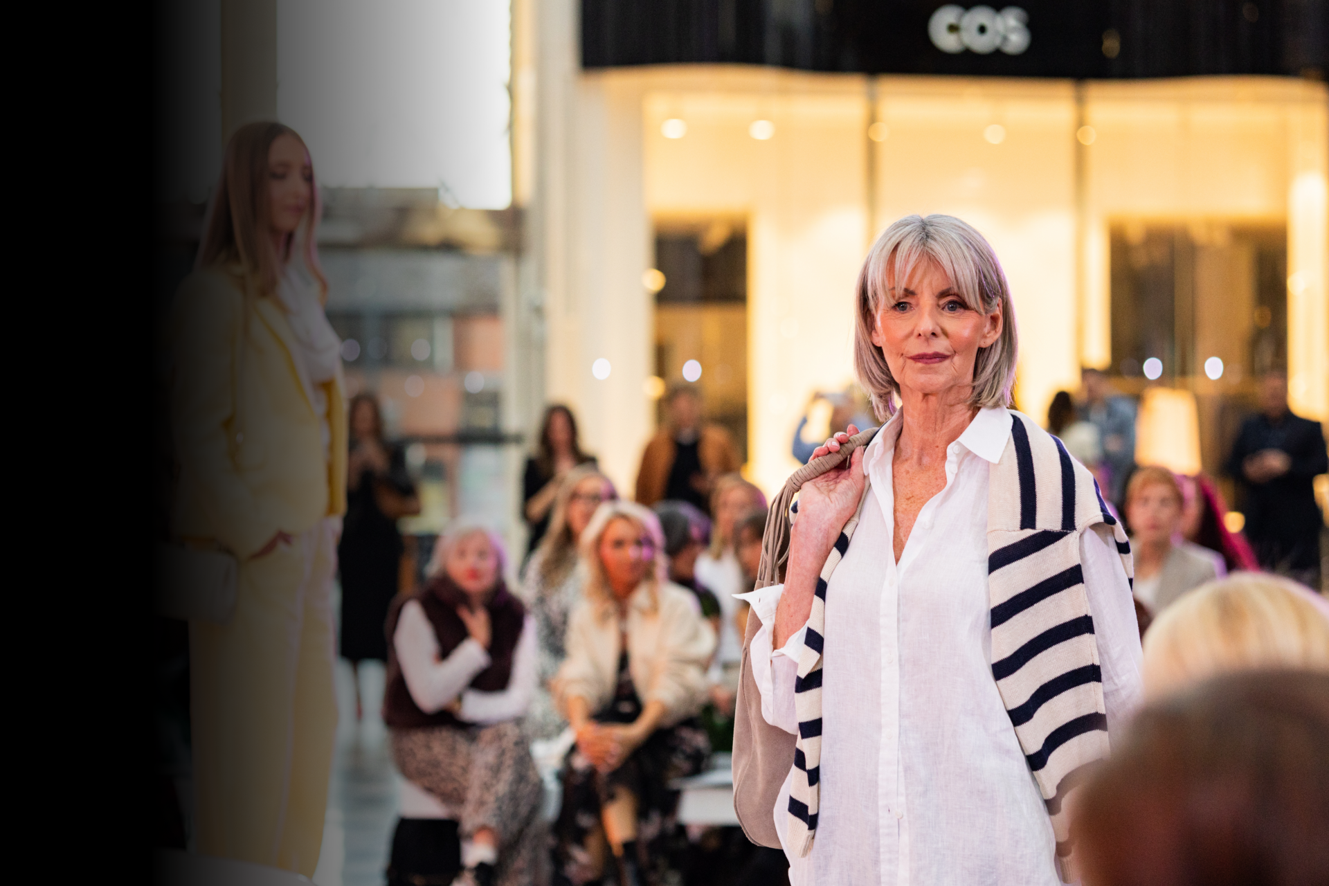 Elegant older woman posing at Victoria Leeds shopping centre, surrounded by shoppers and luxury reta.