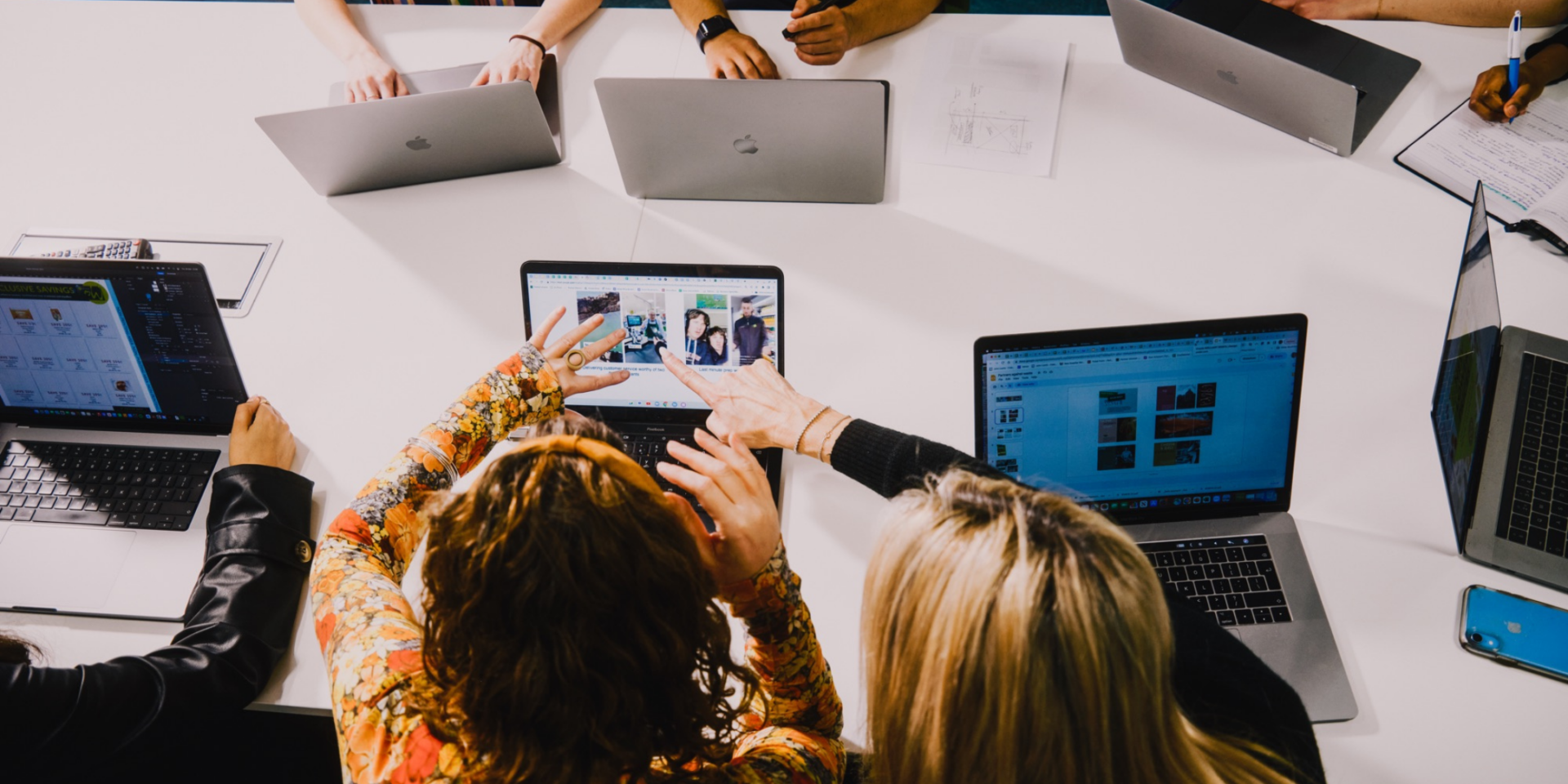 Group of people collaborating around a table with laptops during a tech meeting.
